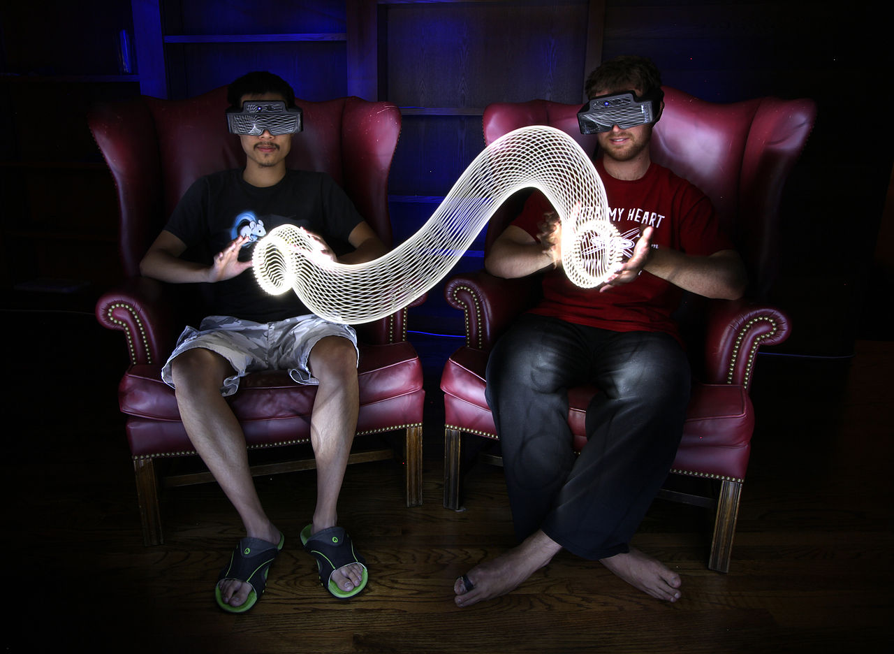 future gaming system concept shows two 20ish men with VR glasses on sitting beside each other.