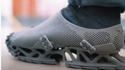 A closeup from the side shows a person wearing a gray shoe. The top looks like a sock with vent holes all around and the sole is partly open with struts at different angles supporting the shoe.