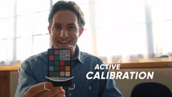 A person with brightly lit windows behind, is holding up a small card with multi-colored squares and a QR code. The text reads Active Calibration.