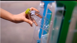 a closeup sideview of a person's hand putting an empty water bottle in one of several different colored trash bins