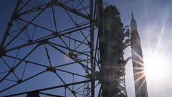 A rocket is on the launchpad with the bright sun behind