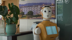 A light-brown and white humanoid robot is seen from the waist up moving through a senior care center.