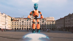 An augmented reality orange and black CGI humanoid robot is floating in the air. The head of the robot is green. Behind the robot is a large building complex on all 3 sides with people walking around in the middle. It is daytime and mostly overcast.