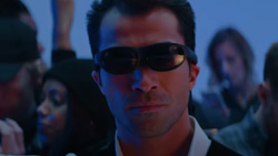 A closeup of a person facing the camera wearing dark sunglasses.