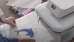 A person is placing an iron-on decal of a dolphin on a tshirt