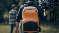 A view from the back of a person wearing an orange and black hard-case backpack