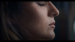 A closeup of a person meditating with eyes closed. The view is of the right side of the face with a dark background.