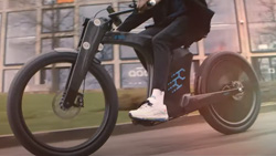 A closeup of a person riding a carbon black ebike in front of a panel-windowed building