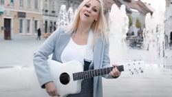 A person is playing a white acoustic guitar on a city street