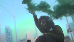 closeup of a protest with a young person on someone's shoulders releasing a green smoke cannister