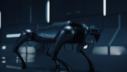 A view in a dark room shows carbon colored quadruped robot. The 'face' is flat with what could be cameras and sensors.