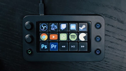 A view from above of a black console with a touchscreen that has color button icons on it. There are 3 knobs on the left and 3 buttons on the right.