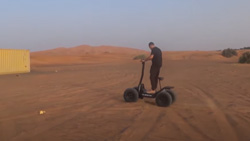 An electric 4 wheel drive scooter shown with a person riding on dirt