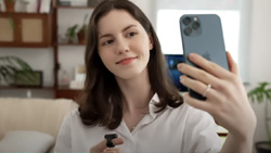 A person facing the camera is taking a selfie. On their other hand is a black device on the index finger