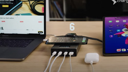 A closeup of a device charger on a desk with 6 devices plugged into it.