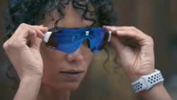 A person is putting on blue sports glasses and wearing a smart watch.