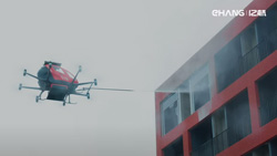 A view from below show a red 8-propeller drone shooting water at a tall red building with windows