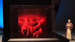 A 3d hologram of Yoda in reddish color. A small statue of Obi-wan sits to the right