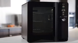 A black square kitchen device sits on a counter. The front shows 3 racks through the glass