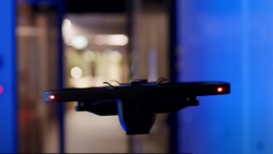 A black drone hovers in a hallway.