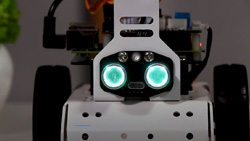 A closeup of a white, boxy, three-wheeled robot with two glowing sensors for eyes.