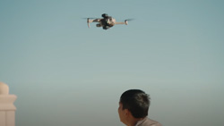 A person looking away from the camera watches a drone flying.