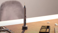 A closeup view of a gray mini pen drill resting vertically in a small stand on a wooden desk. Small drill bits in a holder lay next to it.