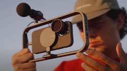 A person is holding an open frame camera mount with a phone, mic and lens attached.