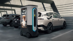 An EV charger sits behind a car in a parking lot. A charging cable is connected to the car from the charger