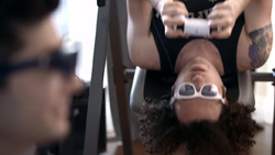 A right-profile of a person in the foreground that is wearing dark XR glasses and another person wearing white XR glasses is hanging upside down with a controller in their hands in the background.