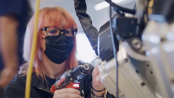 A closeup of a person wearing a black covid mask holding a drill and working on a robot