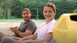 Two people are sitting outside looking and smiling at a small yellow portable air conditioner.