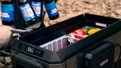 A person is removing bittled drinks from a black and silver cooler. There is an LCD screen mounted at the top of the cooler.