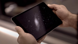 A view from behind and during the day of a person holding a tablet with a galaxy and stars on the screen.