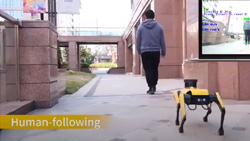 A four-legged robot can be seen following a human that is walking away down a sidewalk