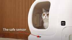 A white rounded enclosure with a tall opening at the front where a gray and white cat sits looking out. A red arrow points to a small black area and the test reads The Safe Sensor.