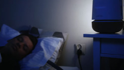 A person is sleeping with a smart cooling pillow pad with a hose attached to a small unit on a night stand