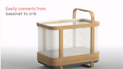 A light colored wood, wth white netting, tall, rectangular baby crib.