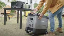 A person is wheeling a large cooler-sized power station in place in a camping setting.