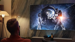 A person sitting watching a large screen TV. The text reads 150 inch and a line is going diagonally across the screen