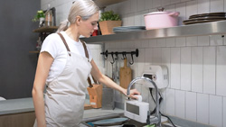 A person wearing an apron is putting a white device in the sink.