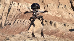A closeup of a black bipedal robot in the air in daylight. Steep mountain terrain is behind. The robot is open framed with a domed head.