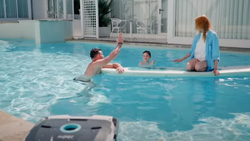 A family is in a large pool with a square pool cleaner in the foreground.