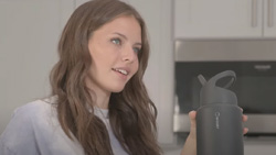 A closeup of a person holding a grey water bottle with a handle and a pop-up straw