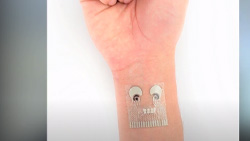 An open-palmed hand and wrist is shown vertically. The wrist has a transparent patch with electronic circuits visible