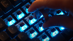 A person is pressing a key on a blue lighted keyboard.