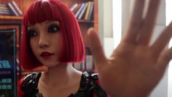 A closeup of a human-looking robot with a short red wig holding a hand up to the camera.